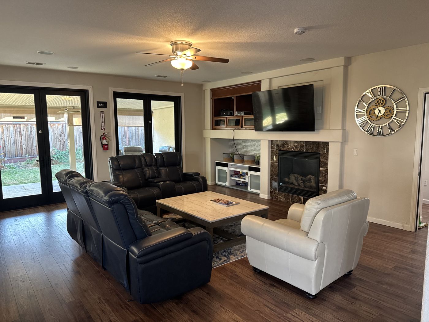 Living room with a tiled fireplace, mounted TV, and doors to the backyard.
