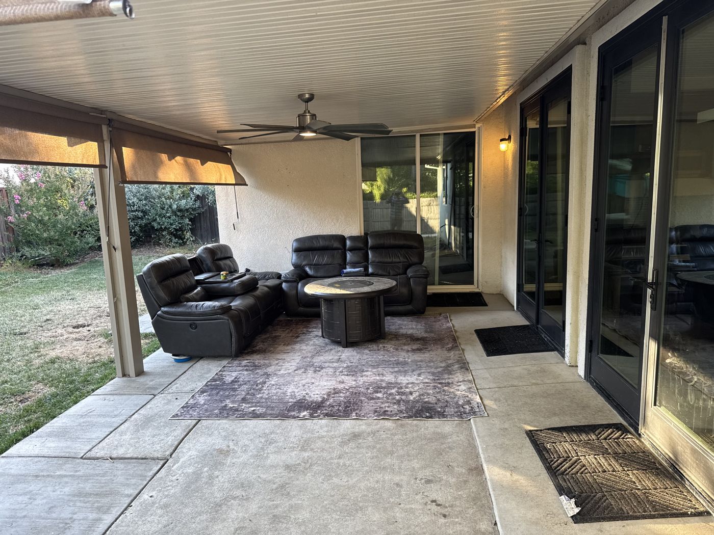 Shaded outdoor sitting area on the back patio with a ceiling fan and garden views.